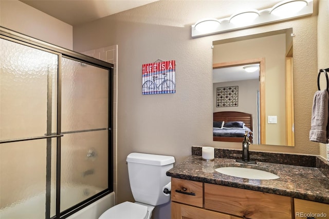 ensuite bathroom with vanity, enclosed tub / shower combo, toilet, and connected bathroom