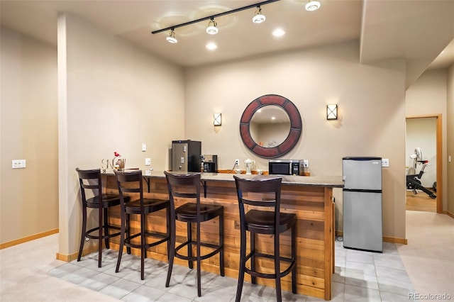 bar featuring stainless steel appliances, wet bar, baseboards, and rail lighting