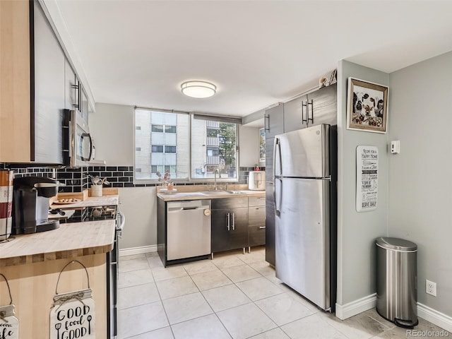 kitchen featuring backsplash, sink, light tile patterned floors, appliances with stainless steel finishes, and butcher block countertops