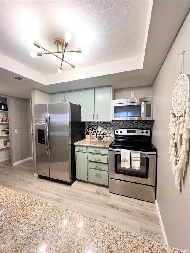 kitchen with a raised ceiling, tasteful backsplash, a textured ceiling, appliances with stainless steel finishes, and light hardwood / wood-style floors