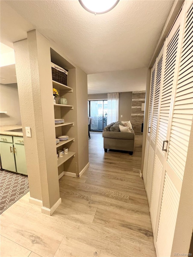 hall featuring light wood-type flooring, a textured ceiling, and built in features