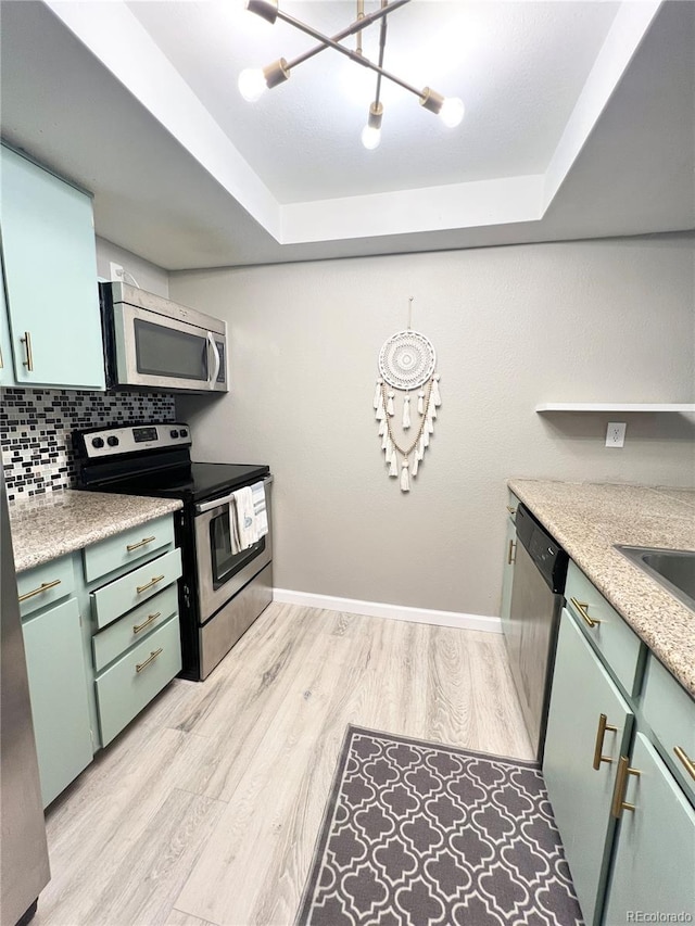 kitchen with light wood-type flooring, a tray ceiling, green cabinetry, stainless steel appliances, and backsplash