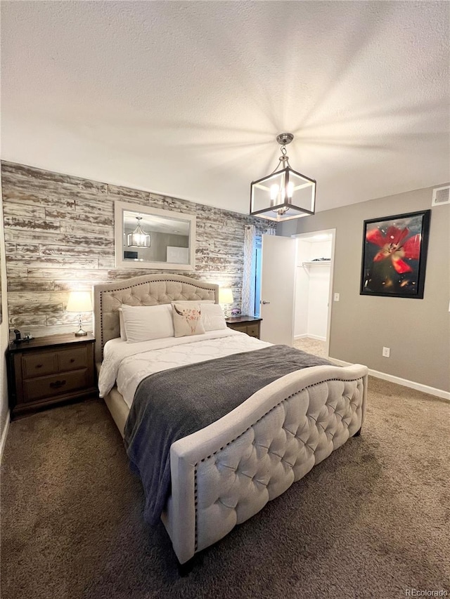 bedroom featuring a textured ceiling, wooden walls, dark colored carpet, and a notable chandelier