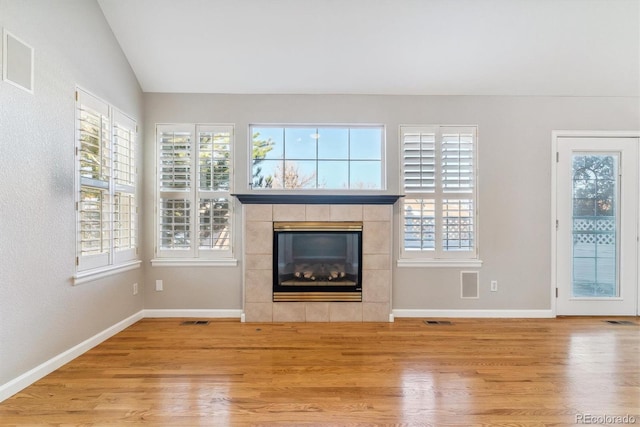 unfurnished living room featuring hardwood / wood-style floors, a healthy amount of sunlight, a tile fireplace, and vaulted ceiling