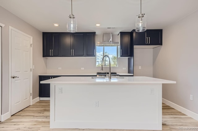 kitchen featuring pendant lighting, sink, an island with sink, and light hardwood / wood-style flooring