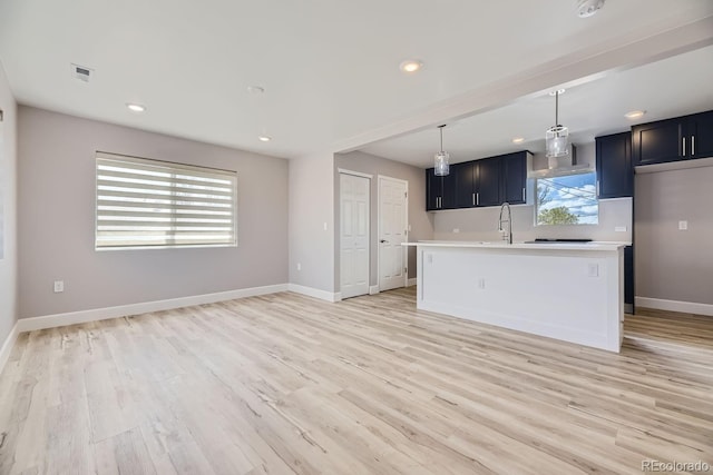 kitchen with pendant lighting, sink, light hardwood / wood-style floors, and a center island with sink