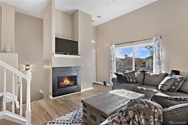 living area with a tile fireplace, wood finished floors, a towering ceiling, baseboards, and stairs