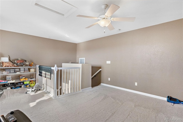 spare room featuring a ceiling fan, attic access, baseboards, and carpet flooring