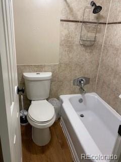 bathroom featuring hardwood / wood-style flooring, toilet, tiled shower / bath combo, and tile walls