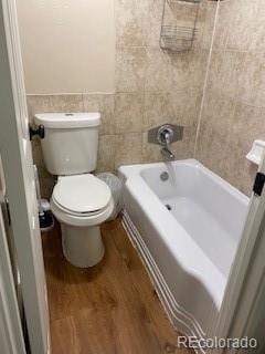 bathroom featuring tile walls, hardwood / wood-style floors, a bath, and toilet