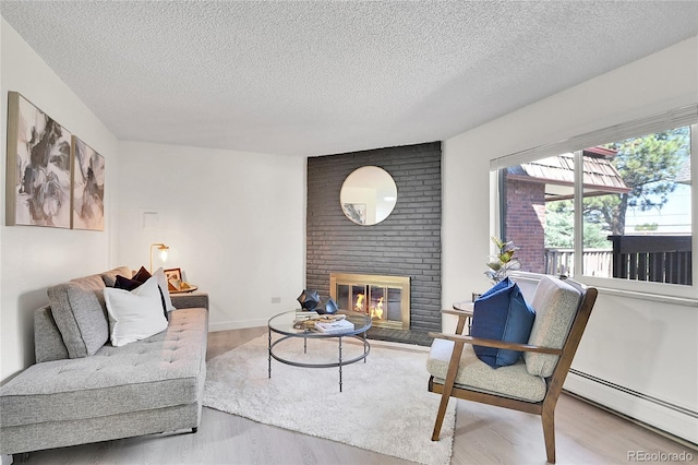 living room with light wood-type flooring, a brick fireplace, a textured ceiling, and a baseboard radiator