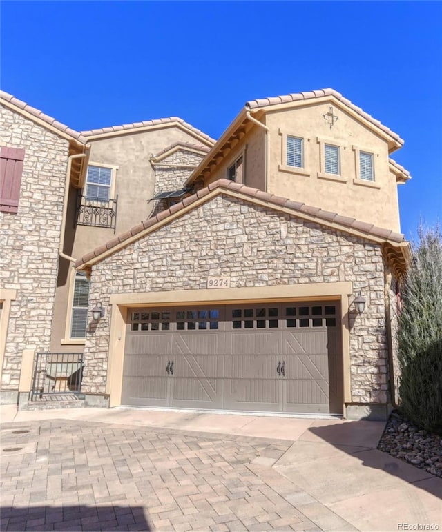 view of front of home featuring stone siding, a tiled roof, decorative driveway, and stucco siding