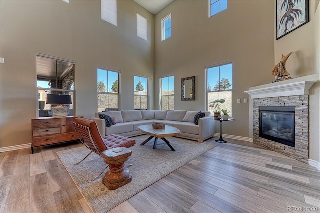 living area with plenty of natural light, a stone fireplace, baseboards, and wood finished floors