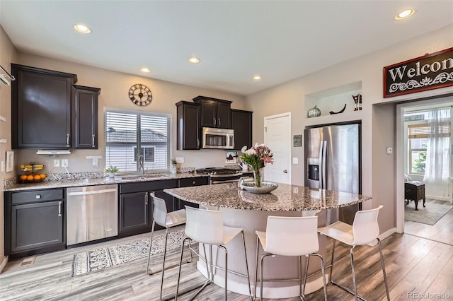 5153 Andes Way, Denver, CO 80249 - kitchen with appliances with stainless steel finishes, recessed lighting, light stone counters, a breakfast bar, and light wood-type flooring