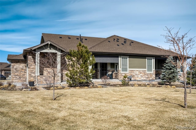 view of front of property featuring a front yard, stone siding, and roof with shingles