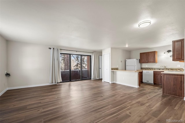 kitchen with baseboards, light countertops, dark wood-type flooring, white appliances, and brown cabinetry