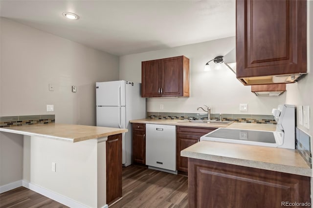 kitchen featuring a sink, light countertops, dark wood-type flooring, white appliances, and a peninsula