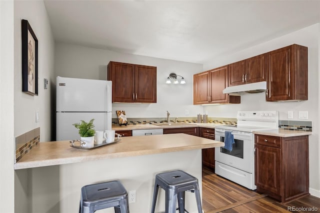 kitchen featuring a kitchen breakfast bar, white appliances, under cabinet range hood, a sink, and dark wood-style floors