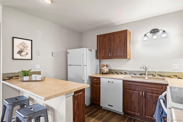 kitchen featuring light countertops, a sink, a kitchen bar, white appliances, and decorative backsplash