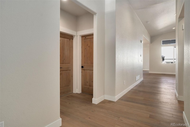 hall with a textured ceiling, vaulted ceiling, and wood-type flooring