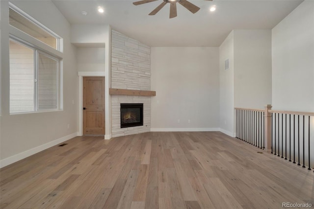 unfurnished living room with a stone fireplace, plenty of natural light, ceiling fan, and light wood-type flooring