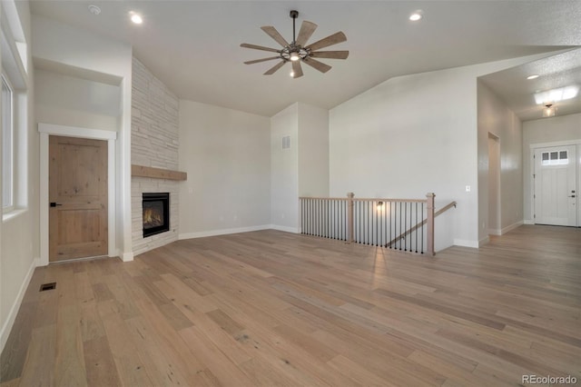 unfurnished living room with ceiling fan, lofted ceiling, a stone fireplace, and light wood-type flooring