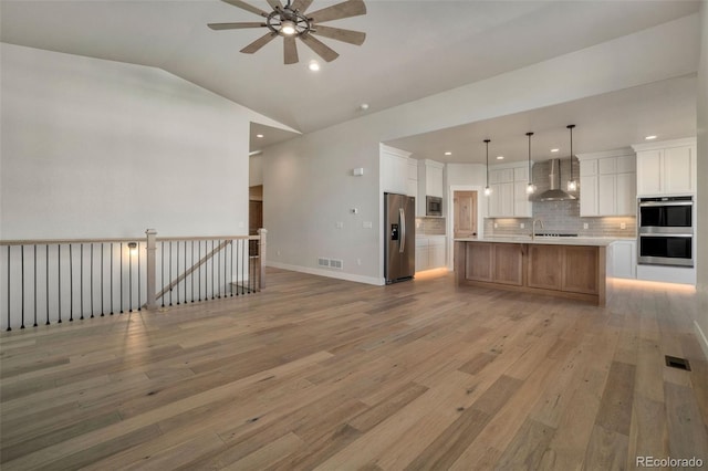 kitchen with vaulted ceiling, a spacious island, white cabinets, stainless steel appliances, and wall chimney exhaust hood