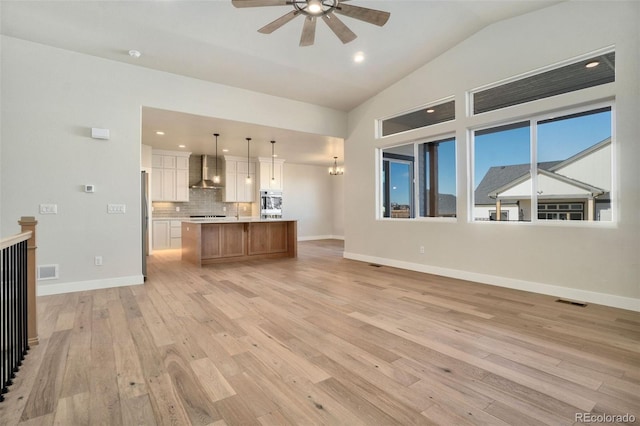 unfurnished living room featuring lofted ceiling, ceiling fan with notable chandelier, and light wood-type flooring