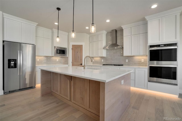 kitchen with white cabinets, an island with sink, wall chimney exhaust hood, and appliances with stainless steel finishes