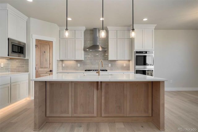 kitchen featuring white cabinetry, appliances with stainless steel finishes, wall chimney exhaust hood, and a kitchen island with sink