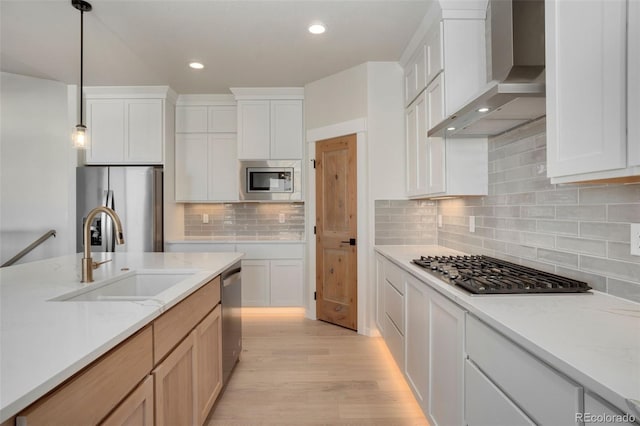 kitchen featuring white cabinetry, wall chimney exhaust hood, stainless steel appliances, and sink