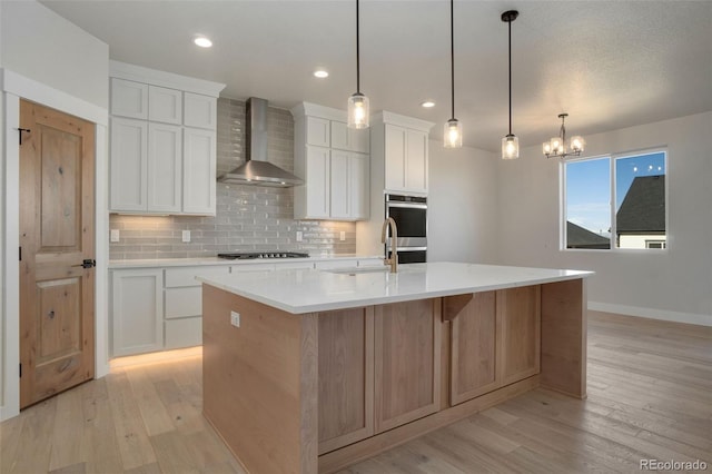 kitchen with white cabinetry, wall chimney exhaust hood, a large island, and hanging light fixtures