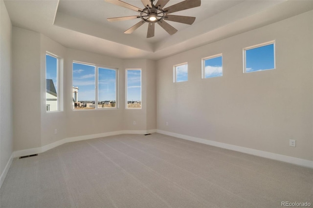 empty room with ceiling fan, light colored carpet, and a raised ceiling