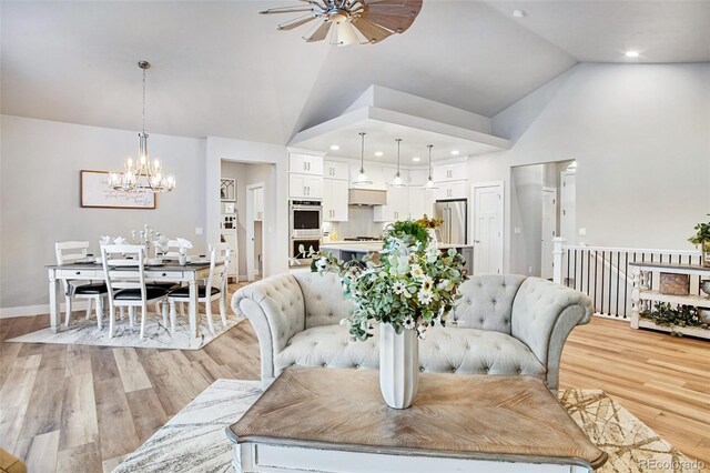 dining area with high vaulted ceiling, ceiling fan with notable chandelier, and light hardwood / wood-style floors