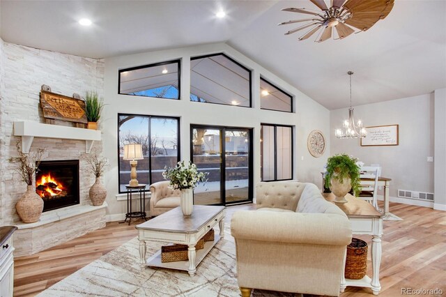 living room with a fireplace, high vaulted ceiling, an inviting chandelier, and light hardwood / wood-style floors