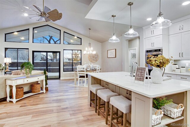 kitchen featuring ceiling fan with notable chandelier, decorative light fixtures, a center island with sink, and white cabinets