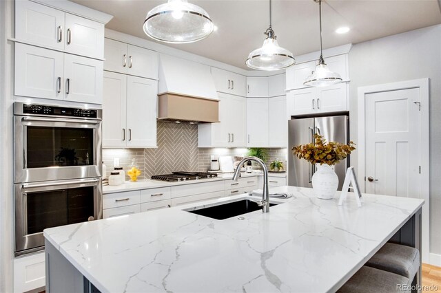 kitchen with hanging light fixtures, stainless steel appliances, sink, and a kitchen island with sink