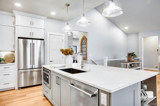 kitchen with light wood-type flooring, stainless steel appliances, white cabinetry, sink, and a center island with sink