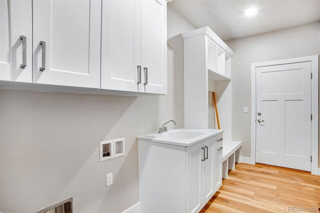 clothes washing area with light hardwood / wood-style flooring, cabinets, sink, and washer hookup