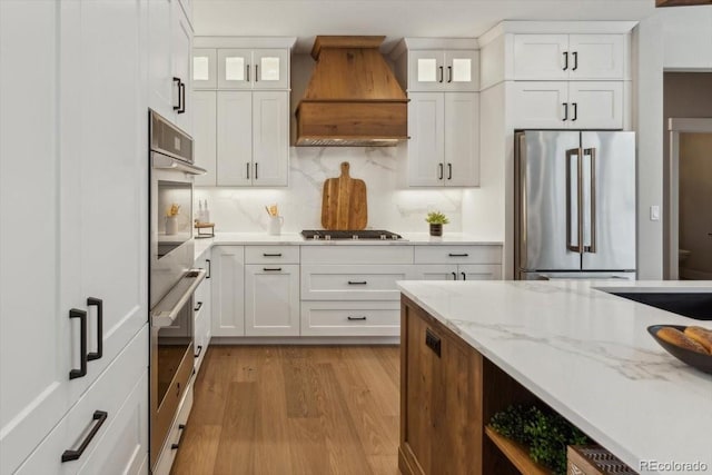 1361 Art Dr, Berthoud, CO 80513 - kitchen with stainless steel appliances, premium range hood, light stone counters, light wood-style floors, and white cabinets
