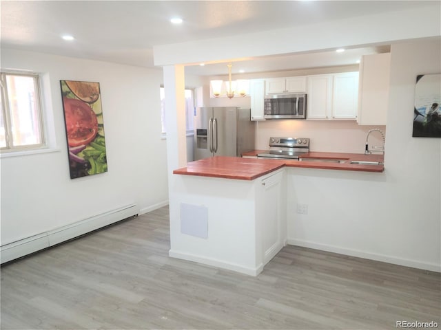 kitchen with appliances with stainless steel finishes, light hardwood / wood-style floors, white cabinetry, and pendant lighting