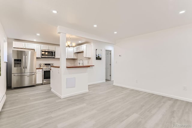 kitchen featuring butcher block countertops, appliances with stainless steel finishes, decorative light fixtures, white cabinets, and light wood-type flooring