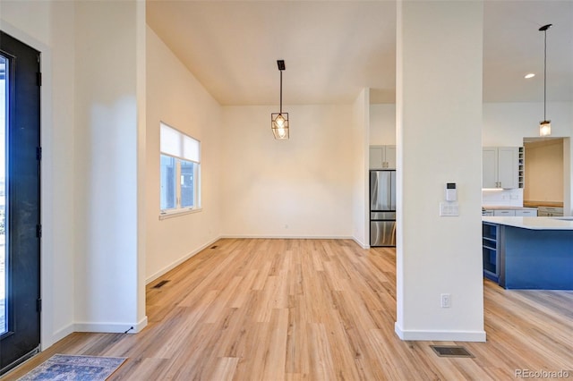 unfurnished dining area featuring light wood-style flooring, visible vents, and baseboards