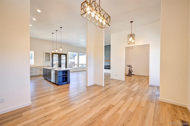 kitchen featuring light countertops, light wood-style flooring, a kitchen island with sink, a sink, and beverage cooler