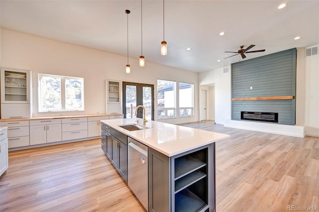 kitchen featuring a large fireplace, stainless steel dishwasher, light wood-type flooring, and a sink