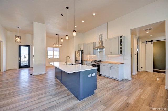 kitchen featuring a barn door, stainless steel appliances, light wood-type flooring, wall chimney exhaust hood, and tasteful backsplash