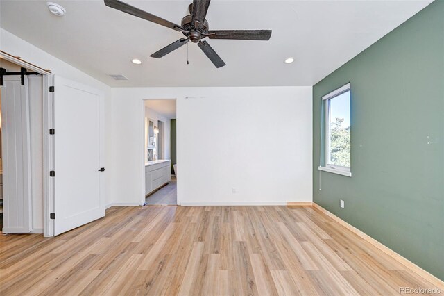 empty room featuring recessed lighting, a barn door, a ceiling fan, light wood-type flooring, and baseboards