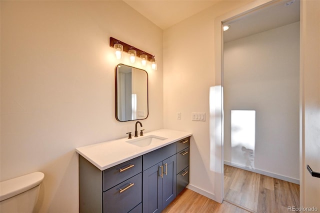 bathroom featuring toilet, baseboards, wood finished floors, and vanity