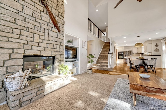 living room with a stone fireplace, built in features, light wood-type flooring, and a towering ceiling