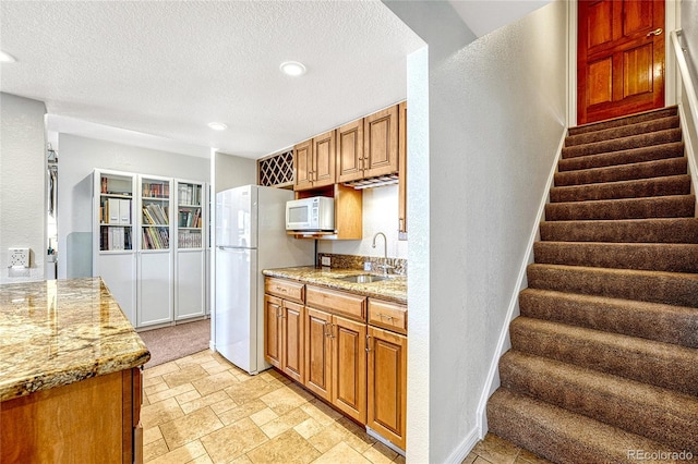 kitchen featuring a textured ceiling, light stone counters, white appliances, and sink